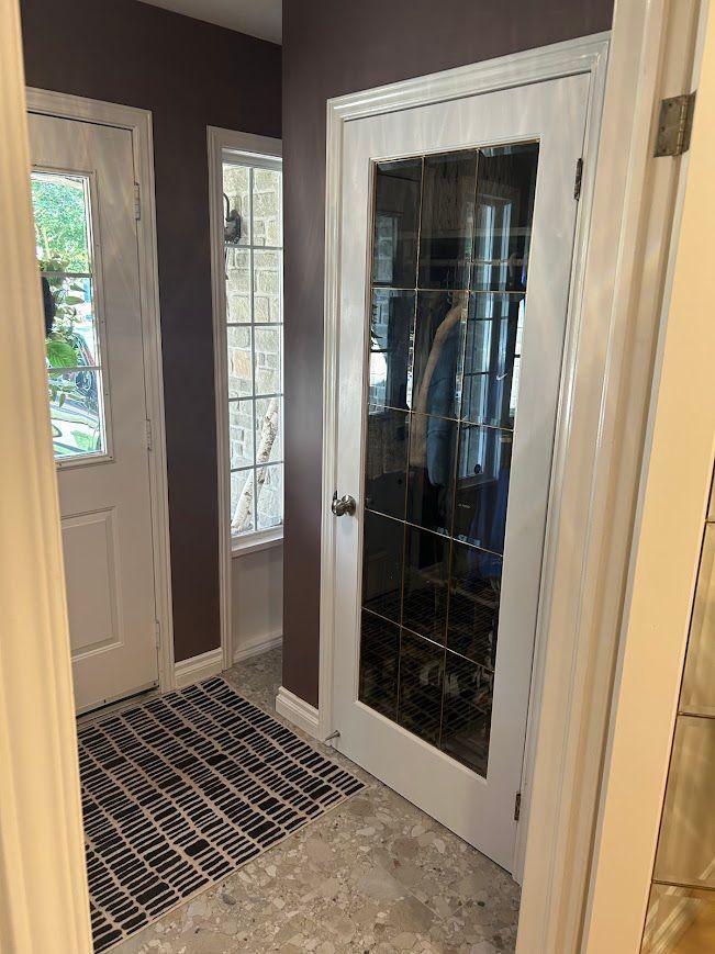 Hallway with a front door, sidelight, and decorative door. Purple walls, white trim, and a patterned rug.