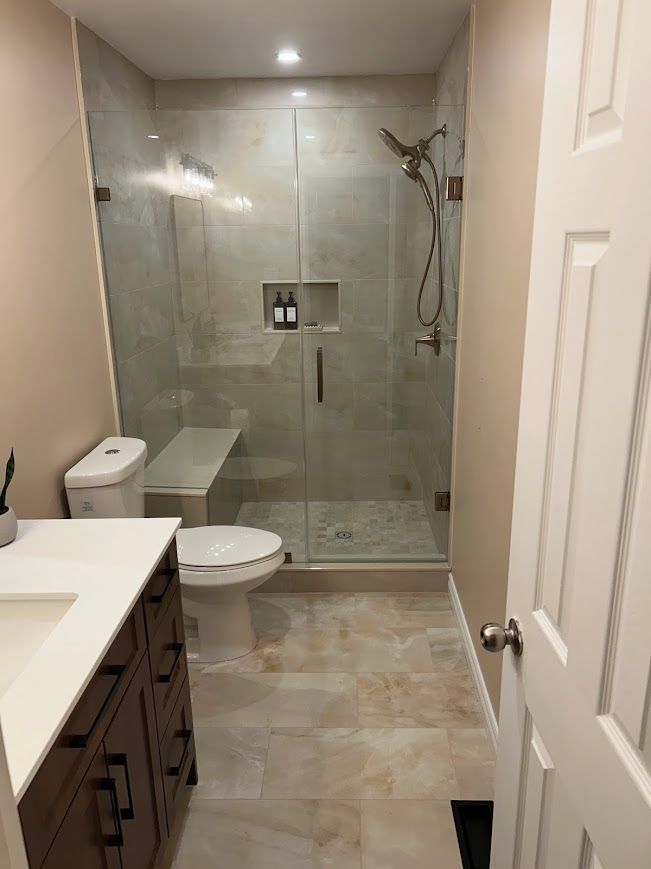 Newly renovated bathroom featuring a glass shower, toilet, vanity, and tan walls.