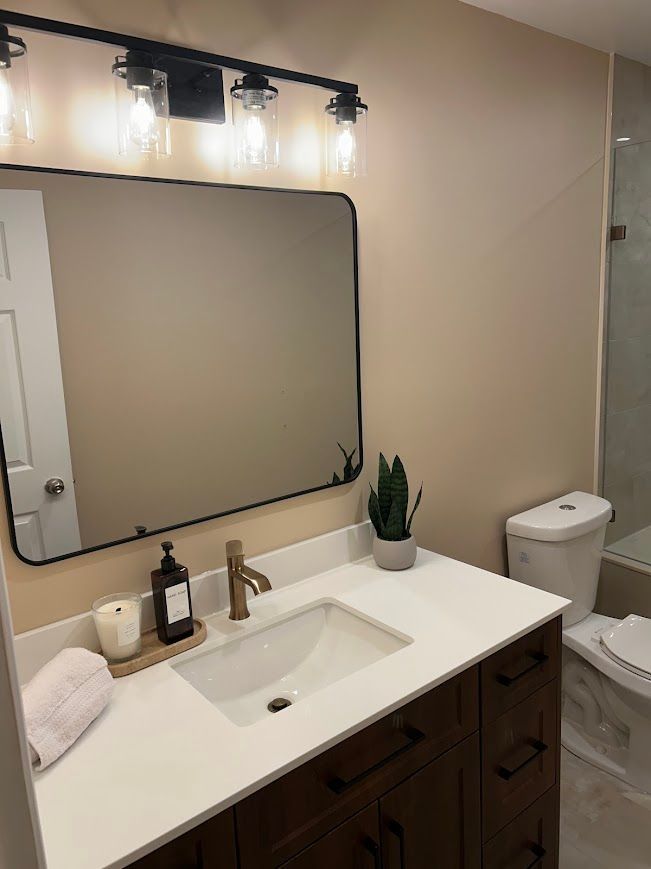 Bathroom with dark wood vanity, white countertop, black-framed mirror, and gold faucet.