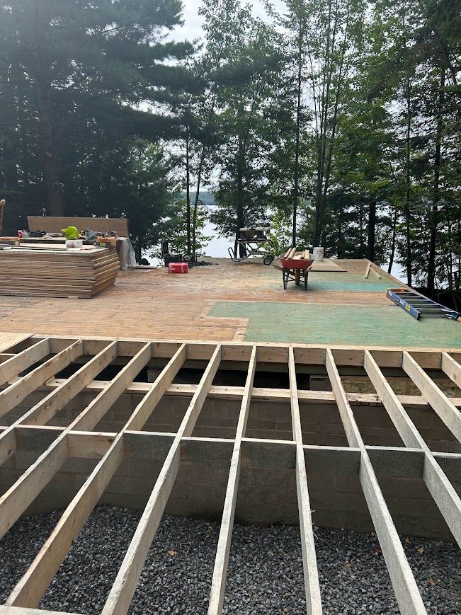 Construction site with wooden floor frame, materials, and a lake view.