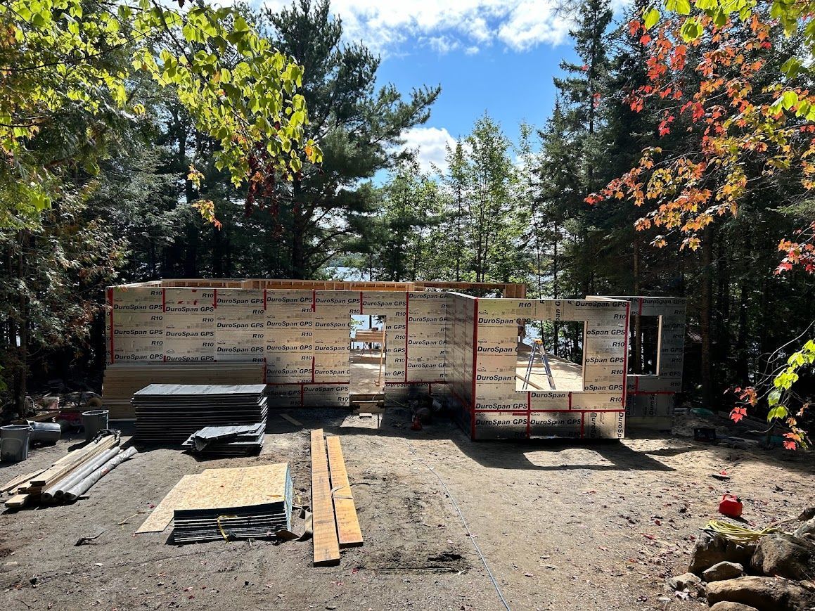 Construction site, a partially built wooden structure surrounded by trees under a blue sky.