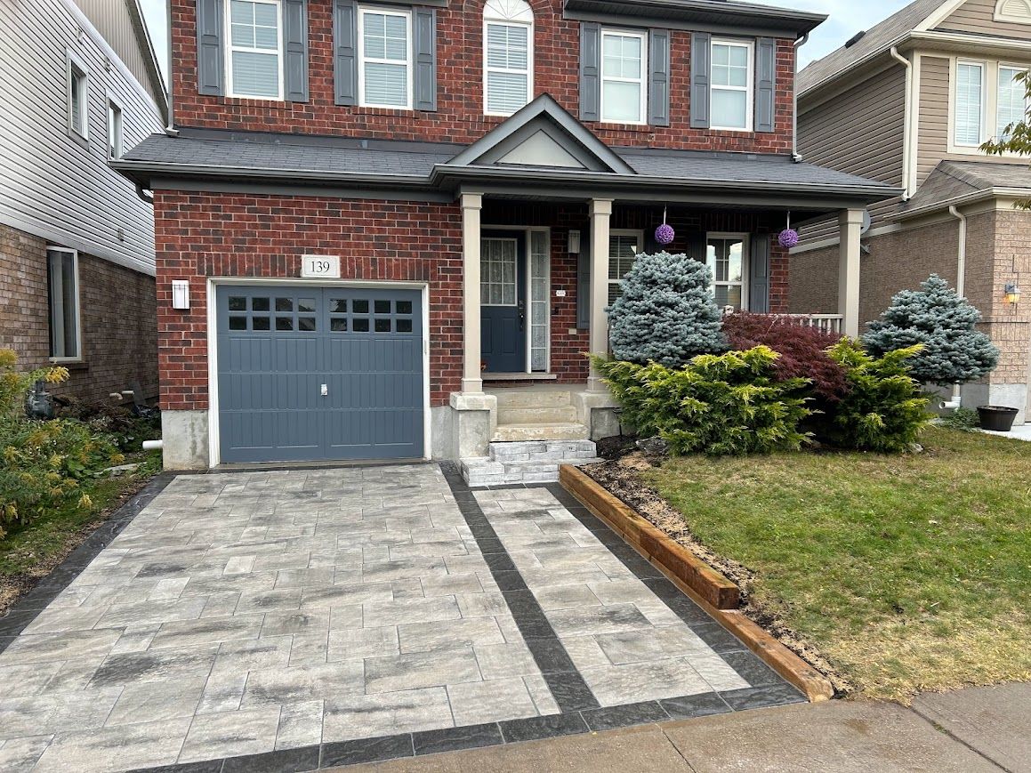 Two-story brick house with gray garage door, paved driveway, small front porch, and landscaping.