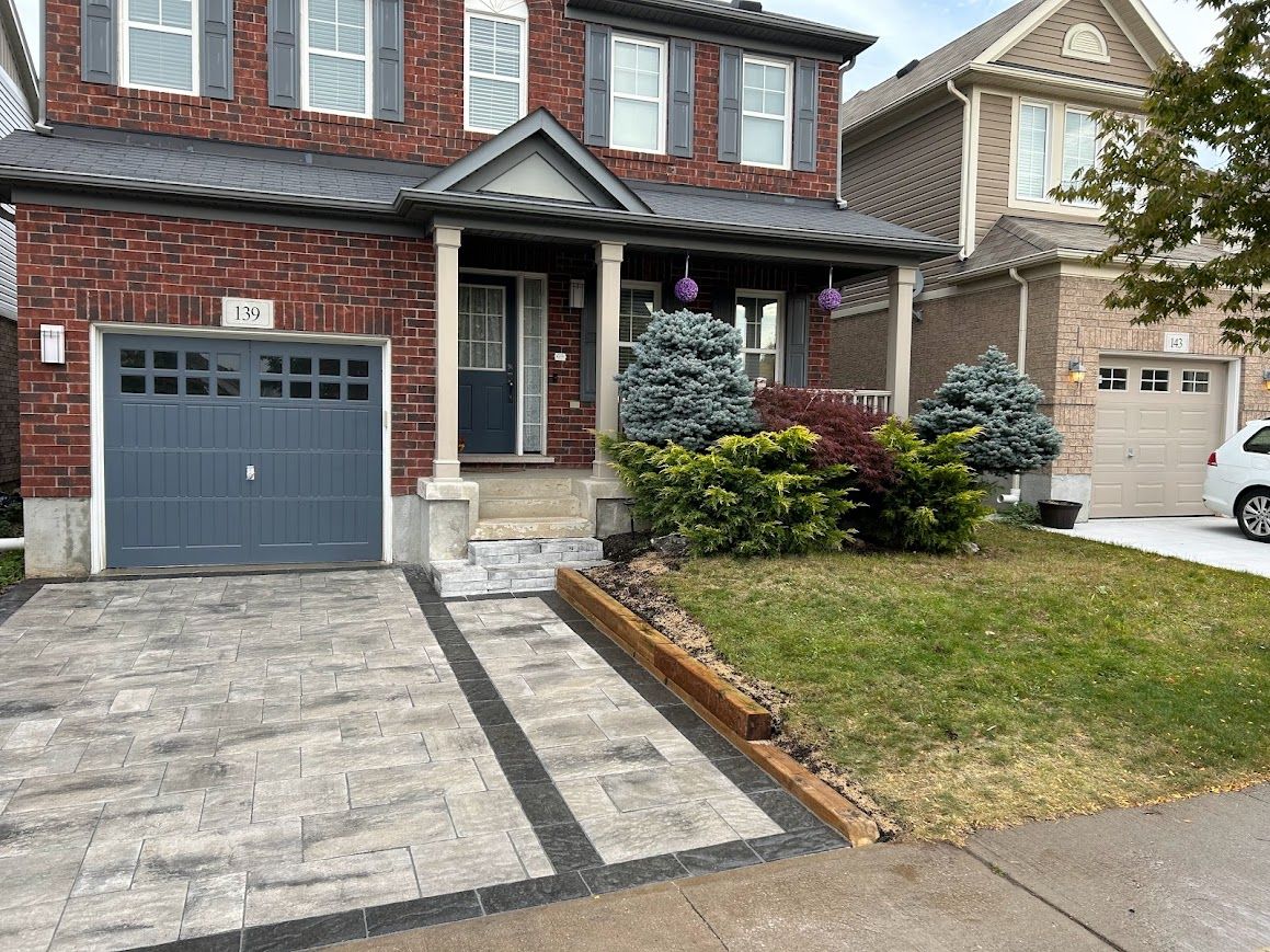 Brick house with blue-gray garage door and driveway, front porch, and small yard with bushes and grass.