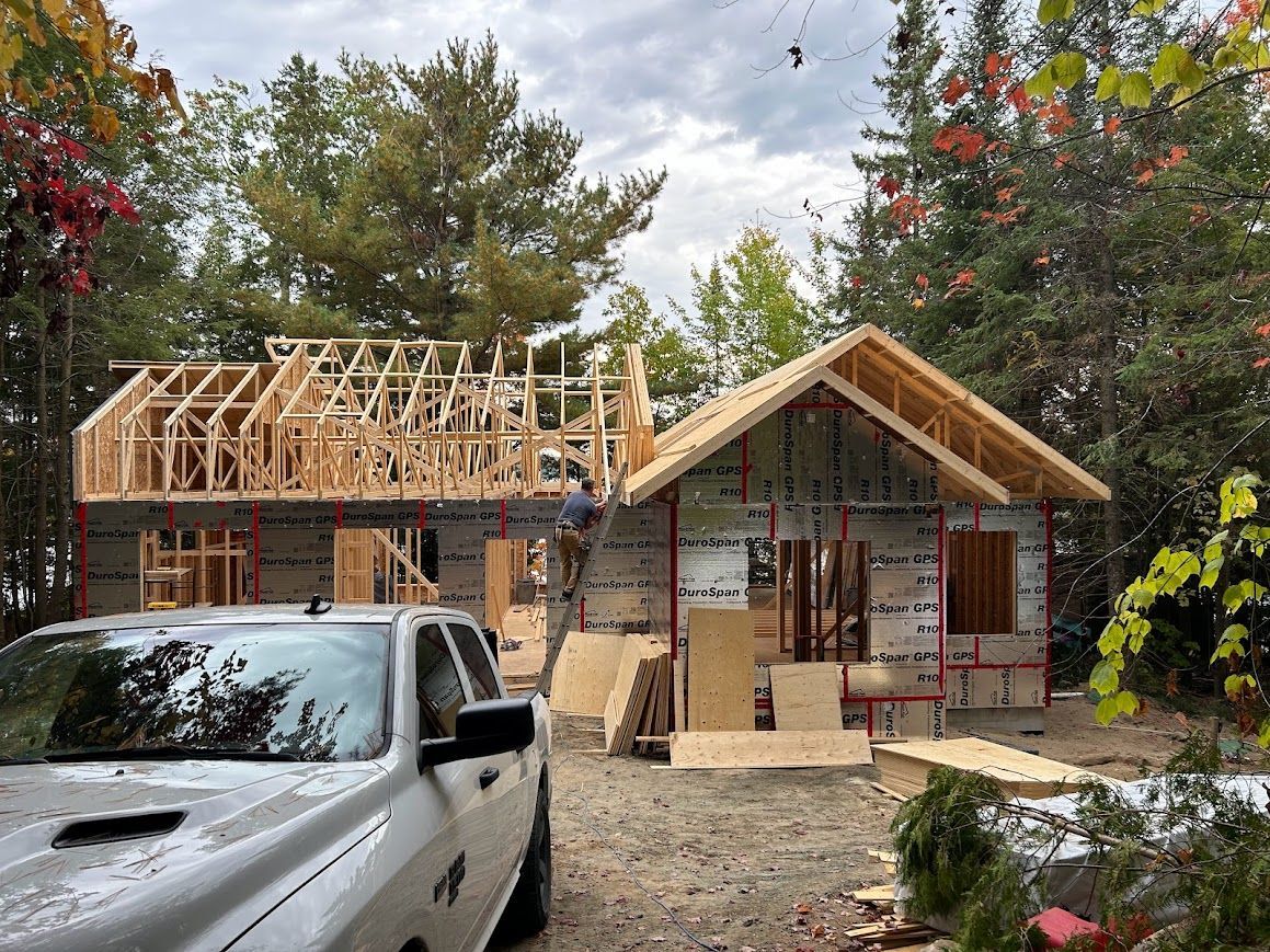 Construction site with a partially built house, framed with wooden beams. Gray truck parked in front.