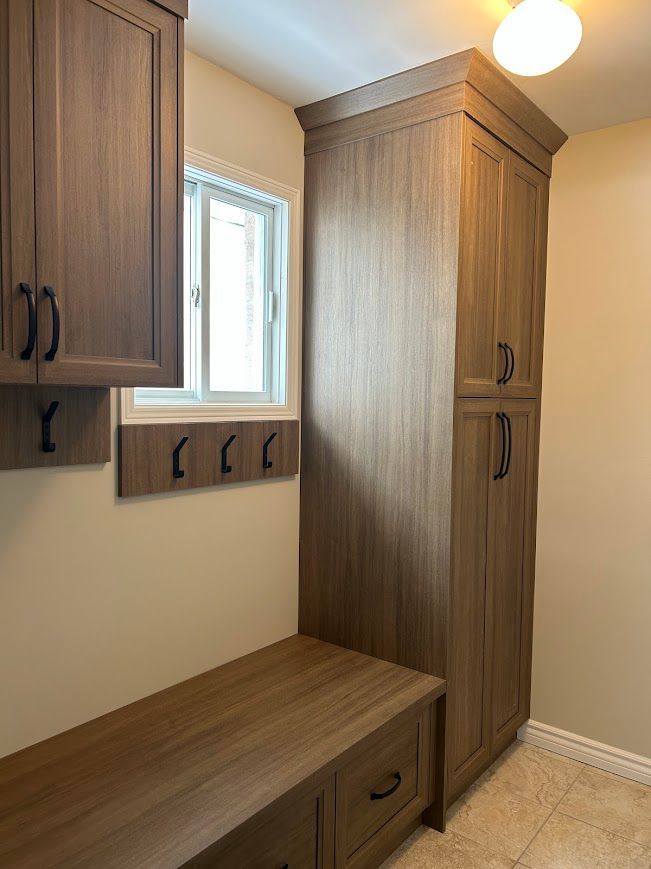 Laundry room with wood cabinets, bench, hooks, and a window.