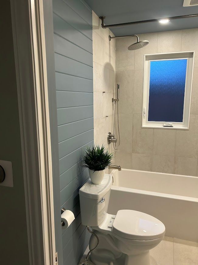 Bathroom with blue wall paneling, toilet, tub, and window.