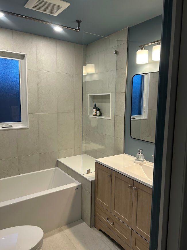 Modern bathroom with a bathtub, vanity, and a glass shower enclosure. Blue walls, light wood vanity, and a white tub.