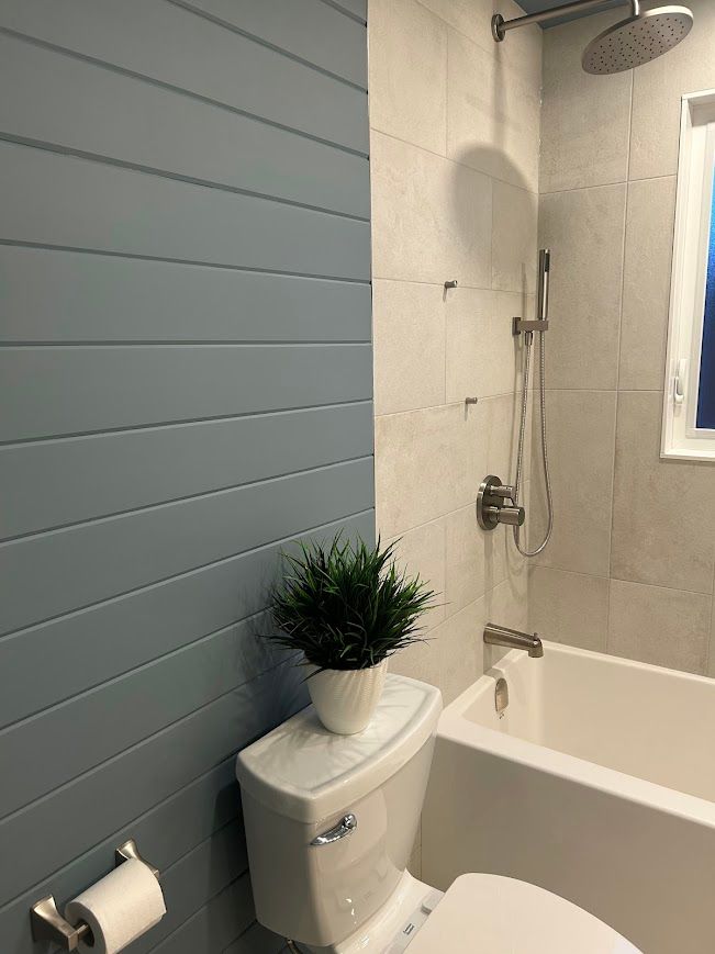 Bathroom with blue shiplap accent wall, white toilet, tub, and tiled shower.