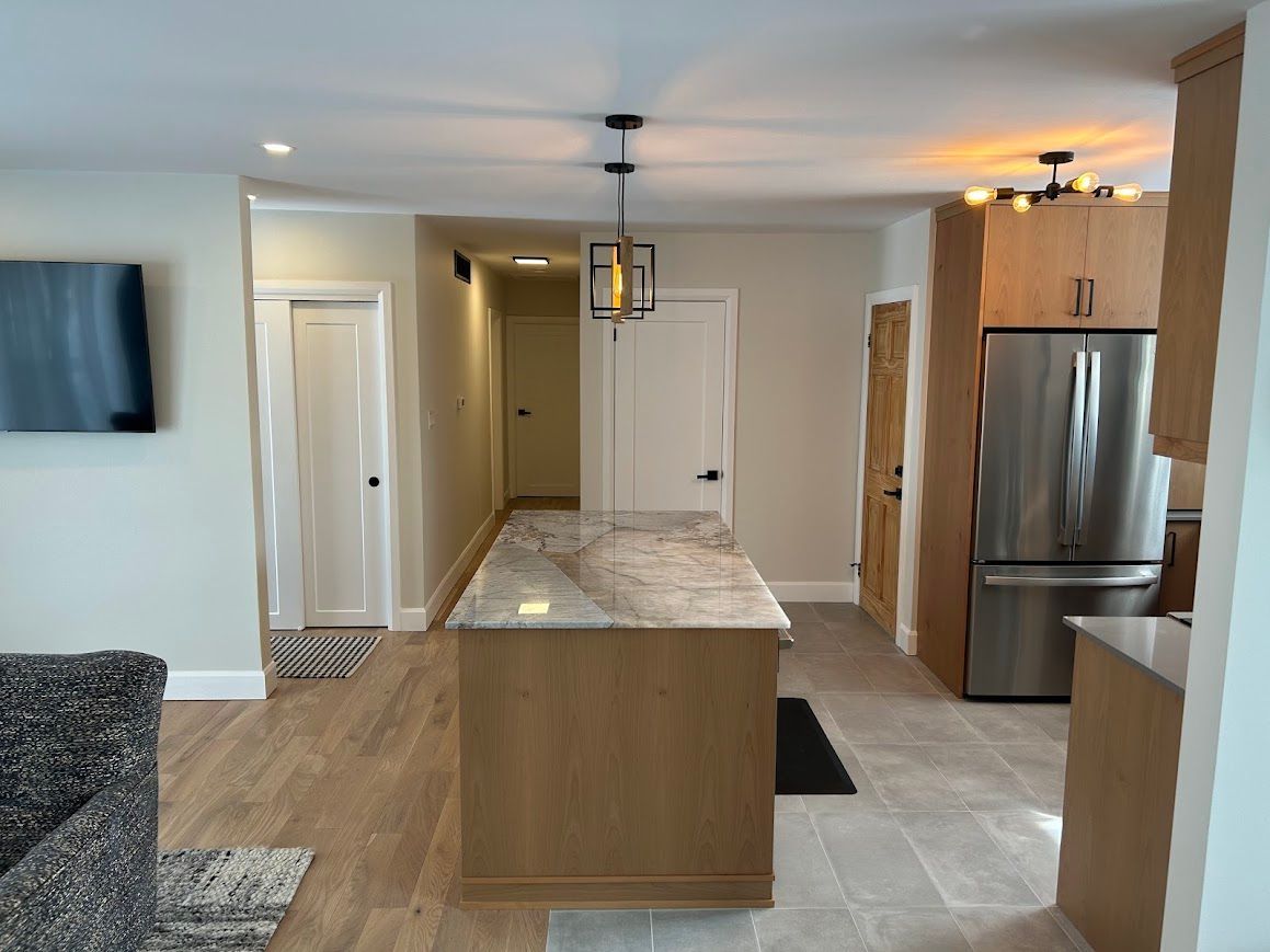 Modern kitchen with light wood cabinetry, stainless steel refrigerator, and a kitchen island with granite countertop.
