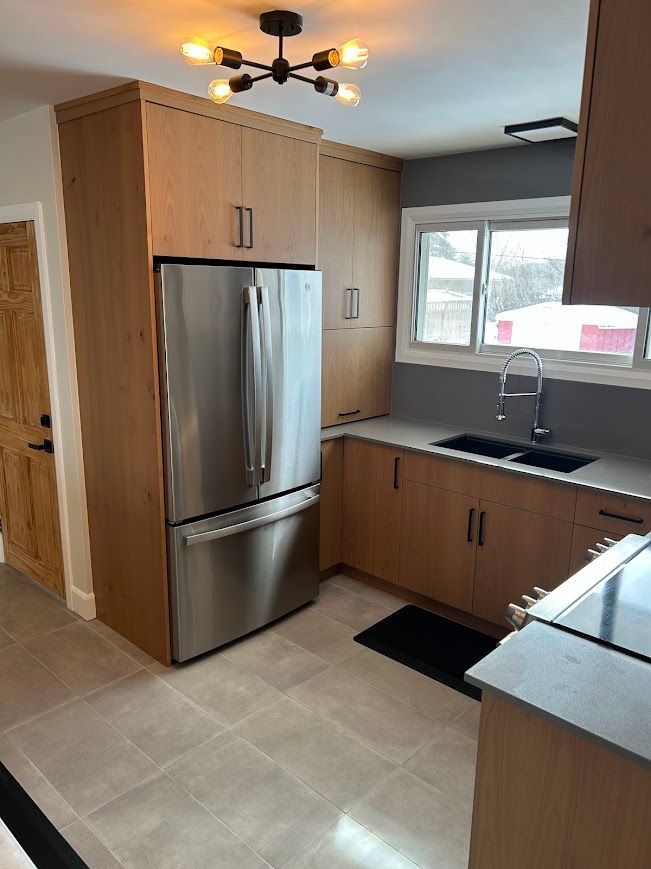 Modern kitchen with stainless steel fridge, light wood cabinets, and gray countertops.