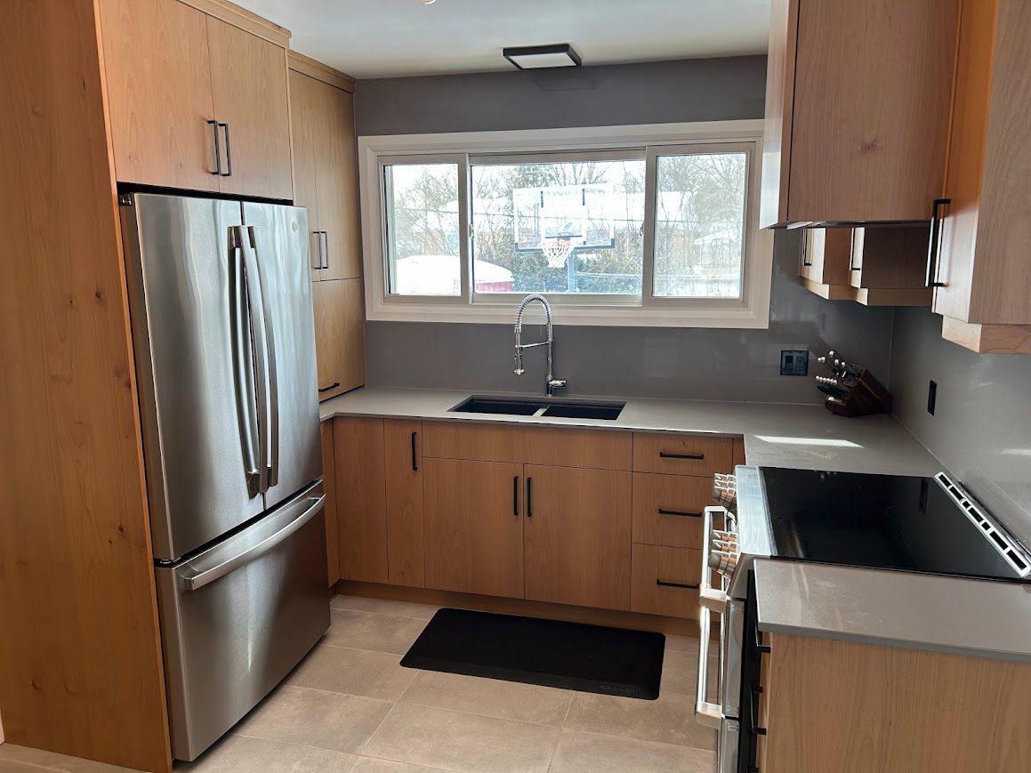 Modern kitchen with light wood cabinets, stainless steel appliances, and a gray countertop.