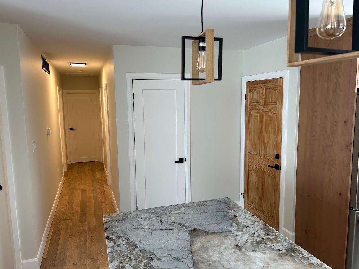 Kitchen interior with granite countertop, wooden floors, white doors, and a decorative light fixture.