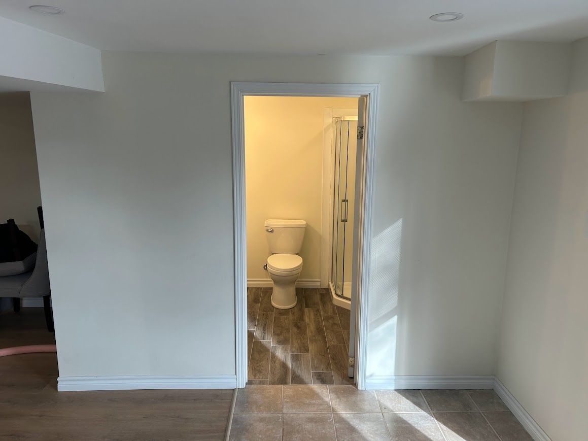 Bathroom doorway; toilet and shower visible inside, beige walls, brown flooring.