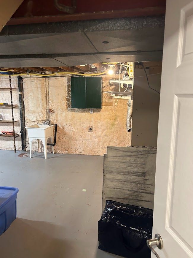 Basement with gray floor, white door open, exposed brick walls, window, utility sink, and shelves.