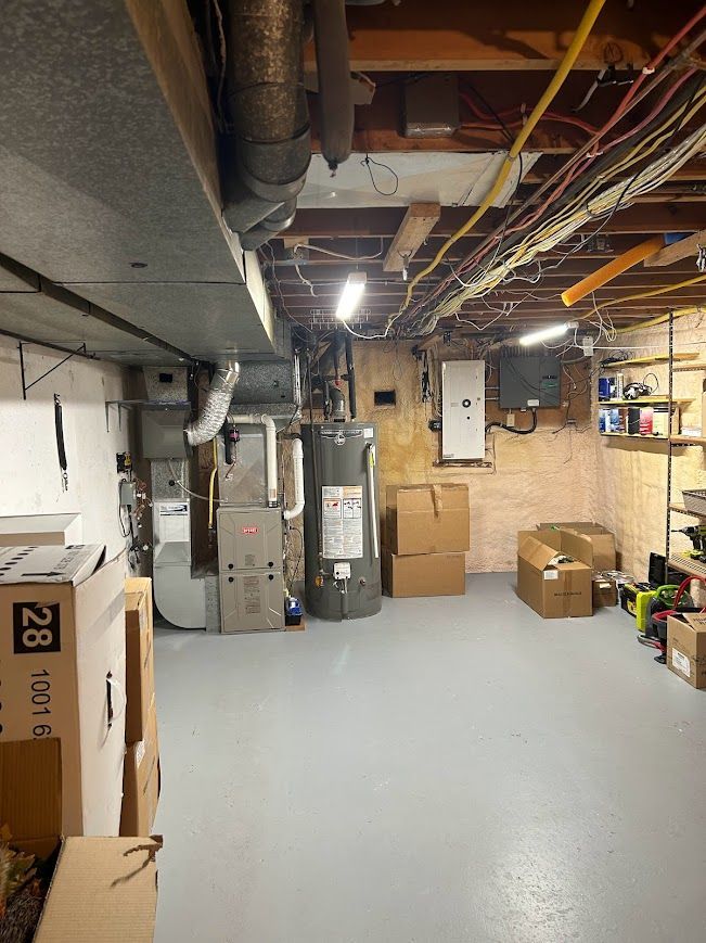 Basement with gray floor, various utilities, boxes, and exposed ceiling fixtures.