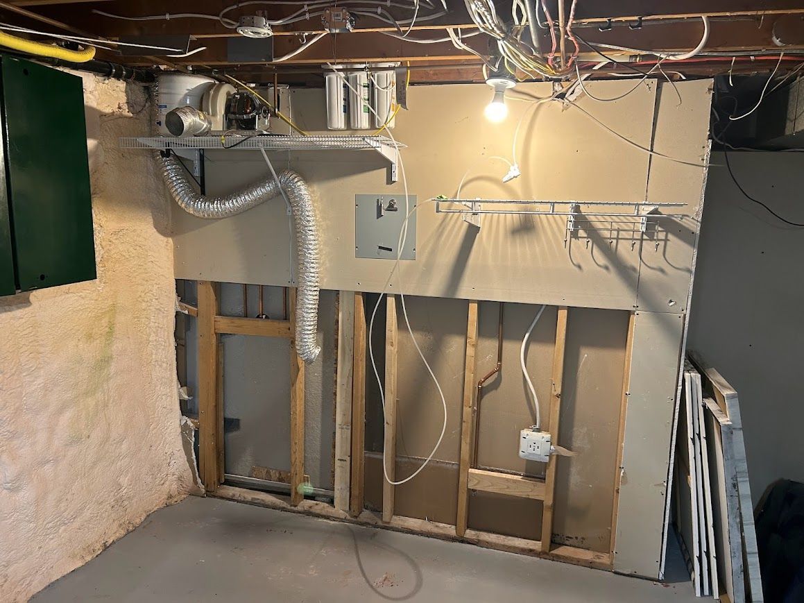 Basement wall under construction: exposed studs, electrical wiring, ductwork, and partially installed drywall.