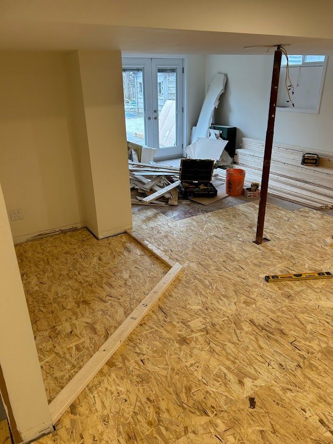 Basement under construction, wooden flooring and support beams. Construction materials and tools are scattered.