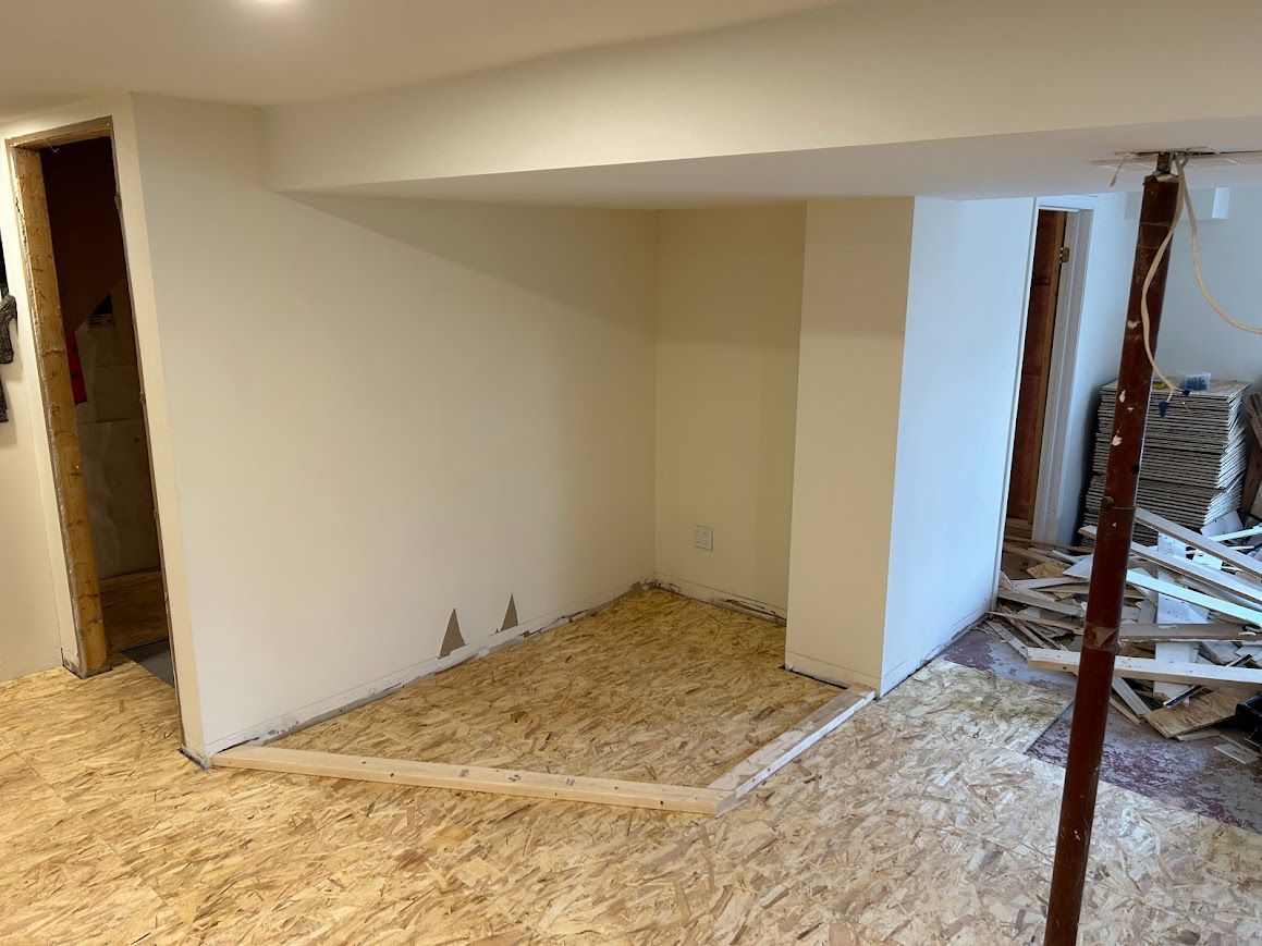 Basement with new plywood flooring installed. Unfinished room with support beam and doorway.