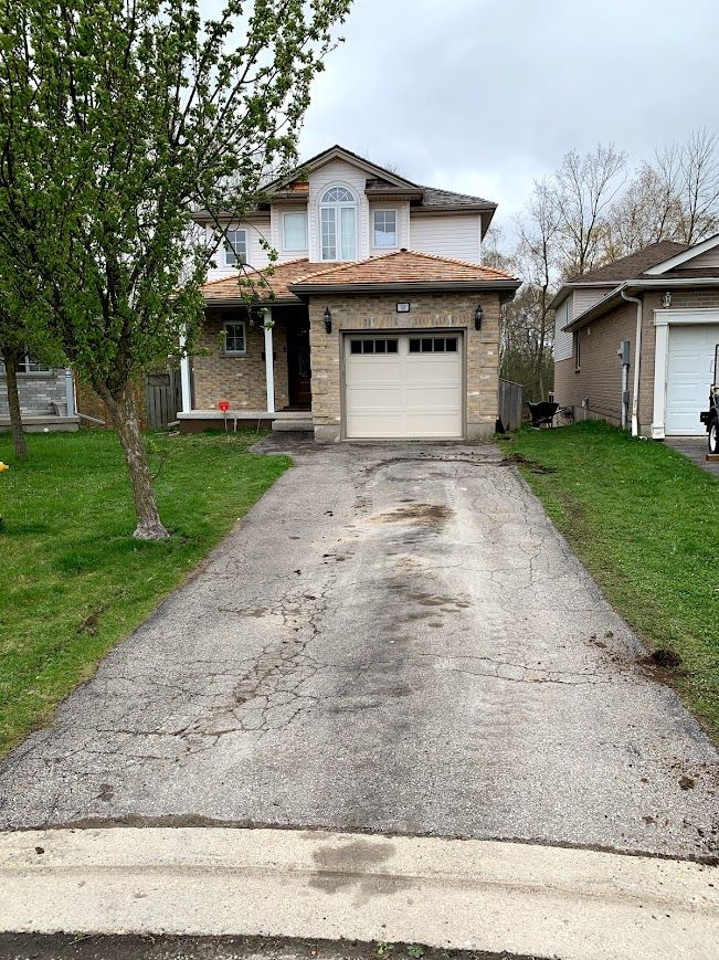 House with damaged driveway, brick facade, and tan garage door. Cloudy sky.