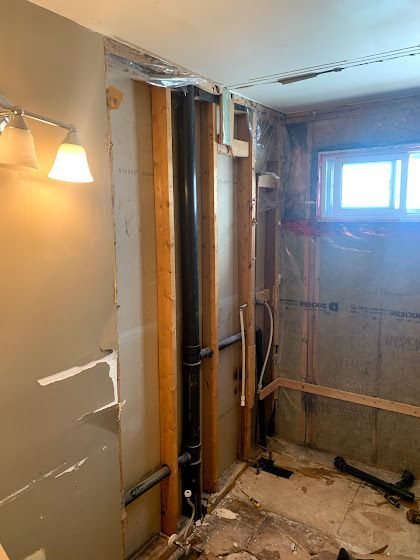 Interior of a bathroom under construction, showing exposed plumbing, studs, and partially removed walls.