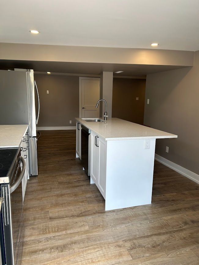 Modern kitchen with white island, stainless steel appliances, and wood-look flooring.