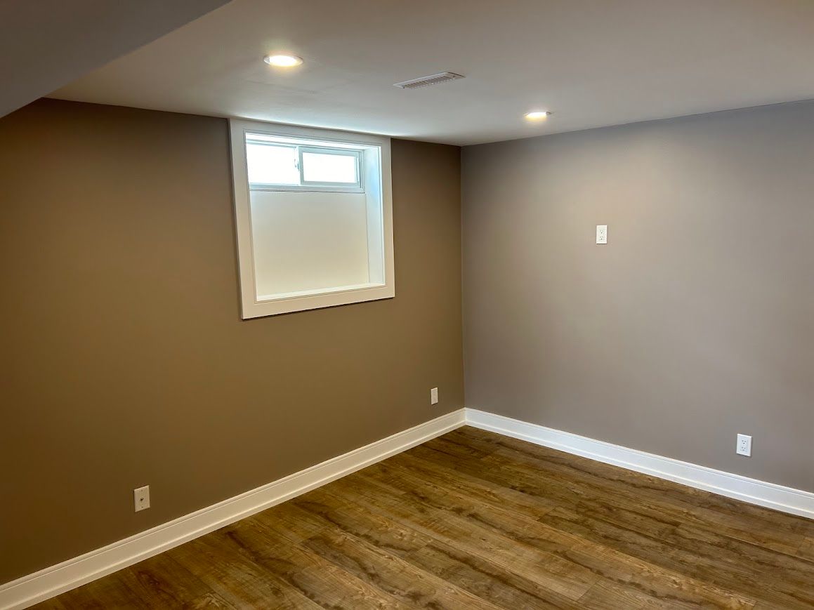 Empty room with brown walls, wood-look flooring, white trim, and a small window.