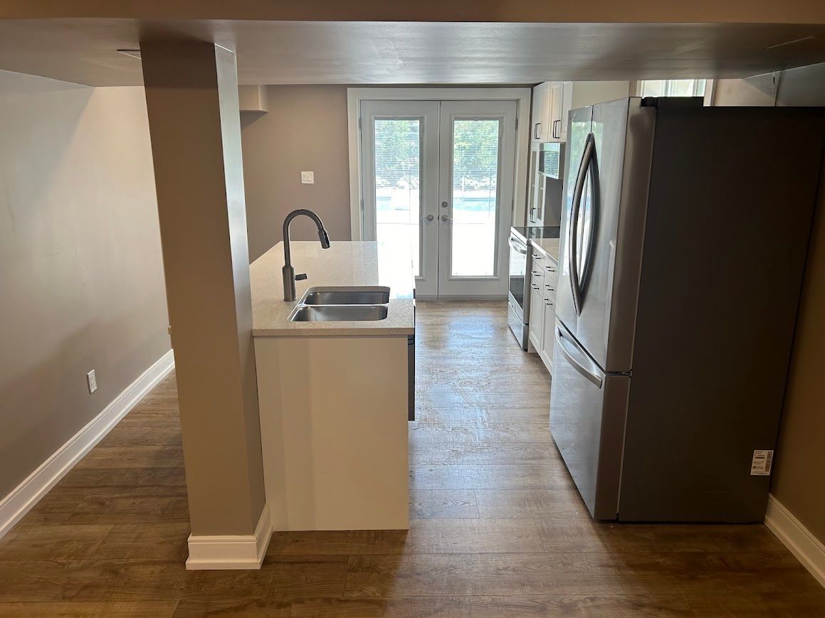 Basement kitchen with white cabinets, stainless steel sink, gray refrigerator, and double doors to outside.