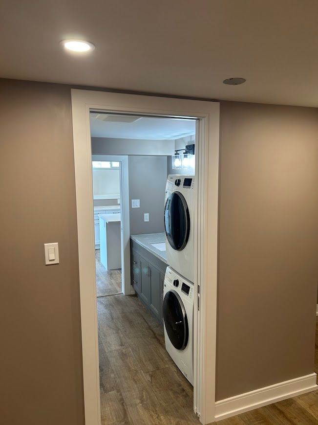 Stacked washer and dryer in a doorway, beige walls, white trim, wood-look flooring.