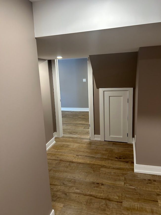 Hallway with wood-look floor, doorways leading to rooms with gray and brown walls, small white door.