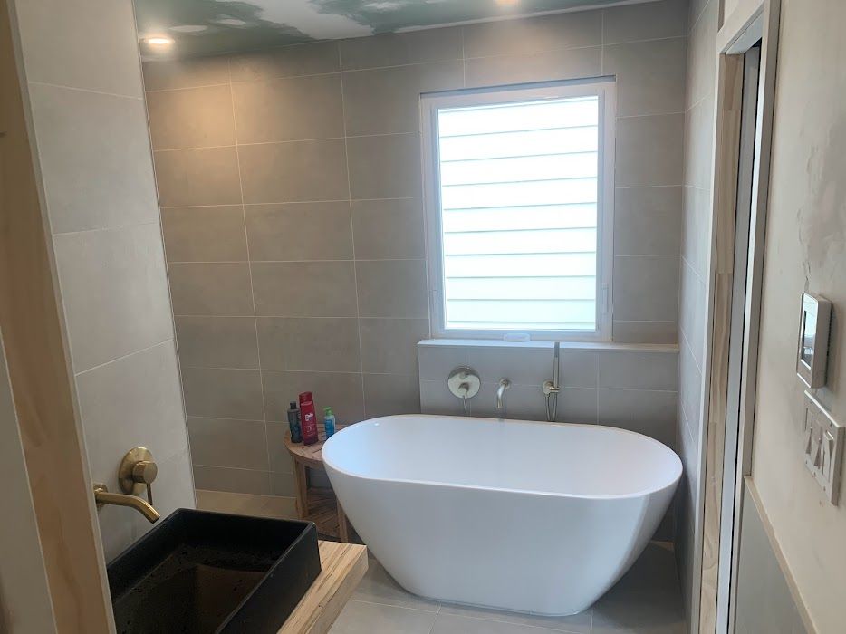 Modern bathroom with a white oval bathtub, tan tiles, and a window.