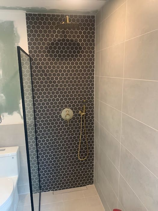 Shower with dark gray honeycomb tile accent wall, gold fixtures, and glass enclosure.