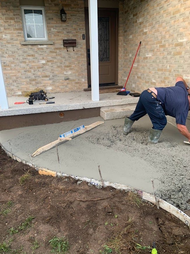 Man smoothing wet concrete sidewalk in front of a brick house.