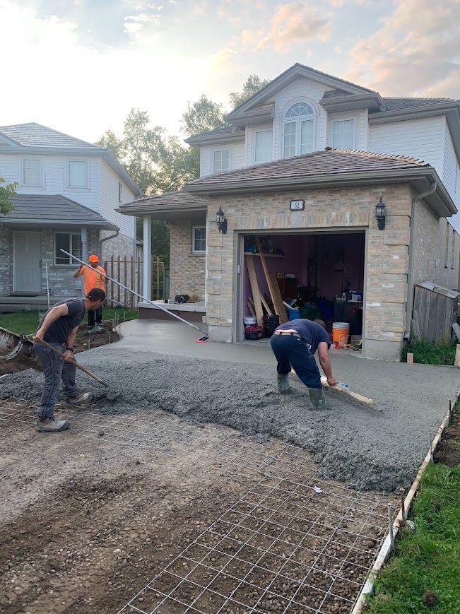 Concrete workers leveling a fresh driveway in front of a house. Two workers on the concrete, one with a rake.
