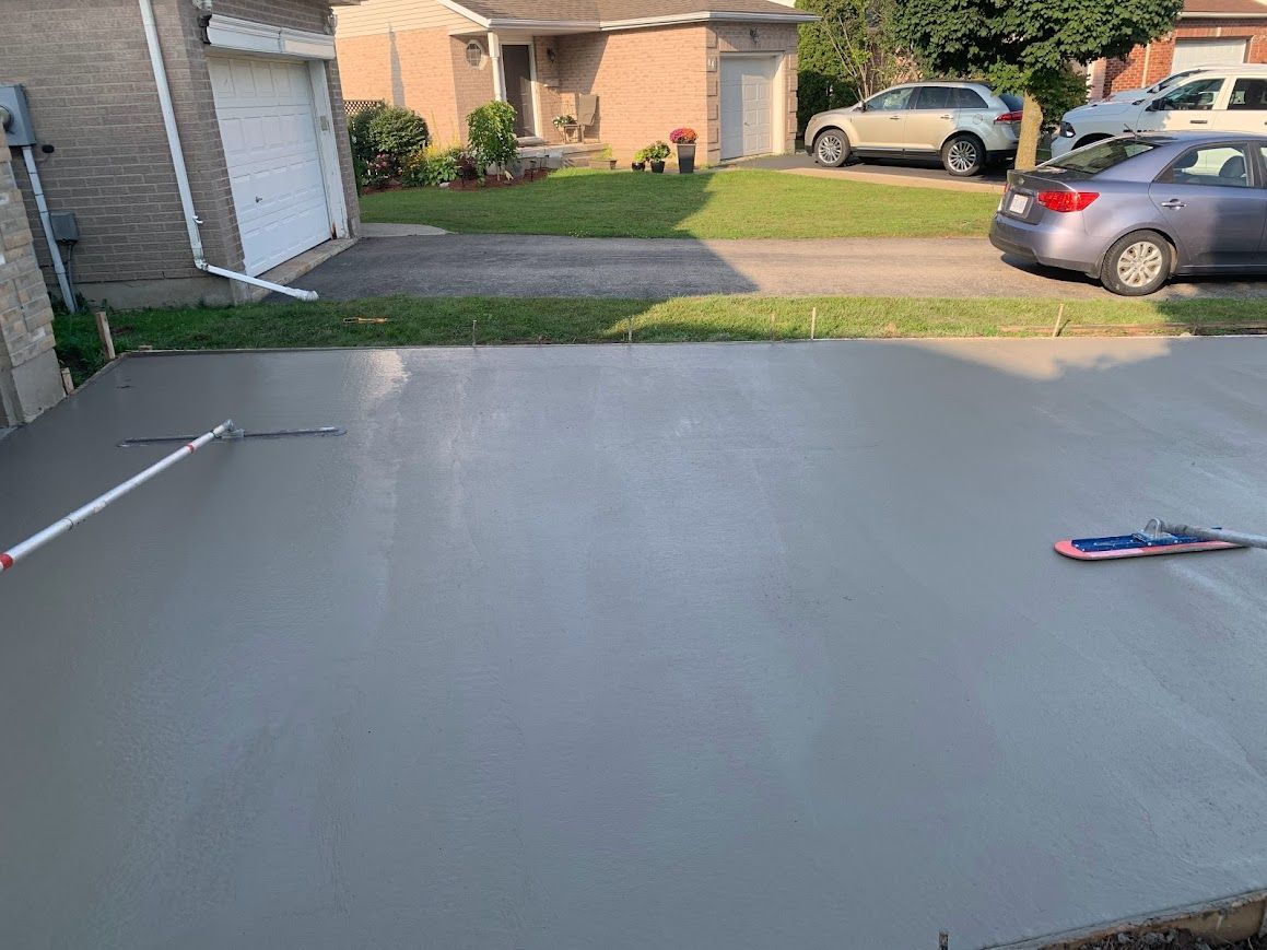 Newly poured gray concrete driveway in front of a house, with parked cars and a lawn visible.