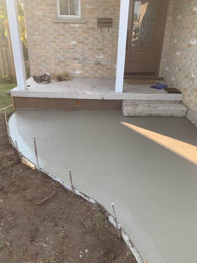 Freshly poured concrete walkway leading to a brick home's porch.