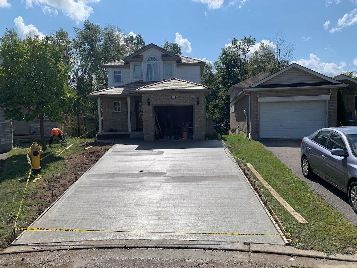 Newly poured concrete driveway in front of a two-story house, sunny day.