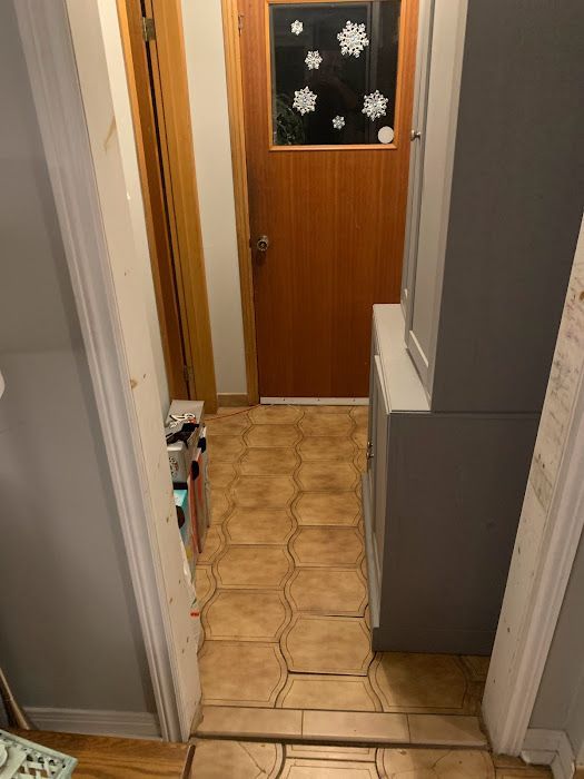 Narrow hallway with hexagonal tile floor, leading to a wooden door decorated with snowflakes.
