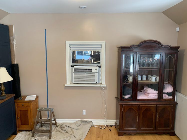 Interior room with tan walls, window with AC unit, and dark wooden hutch. A blue pole stands beside a stepladder.