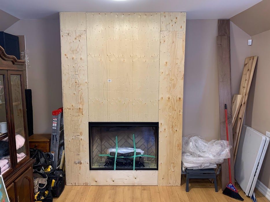 Fireplace being built; wooden surround, black firebox, tools, and materials in room.