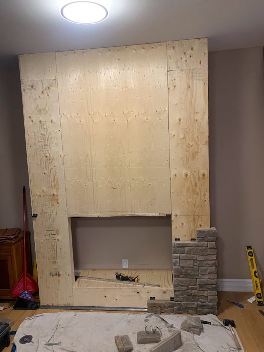 Fireplace under construction, wood frame with stone veneer being applied.
