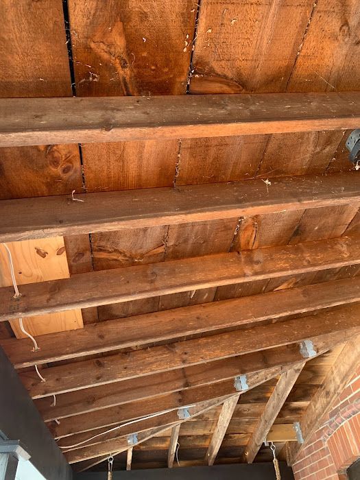 Wooden rafters and boards form a ceiling, possibly of a porch or overhang. Brown wood, visible from below.