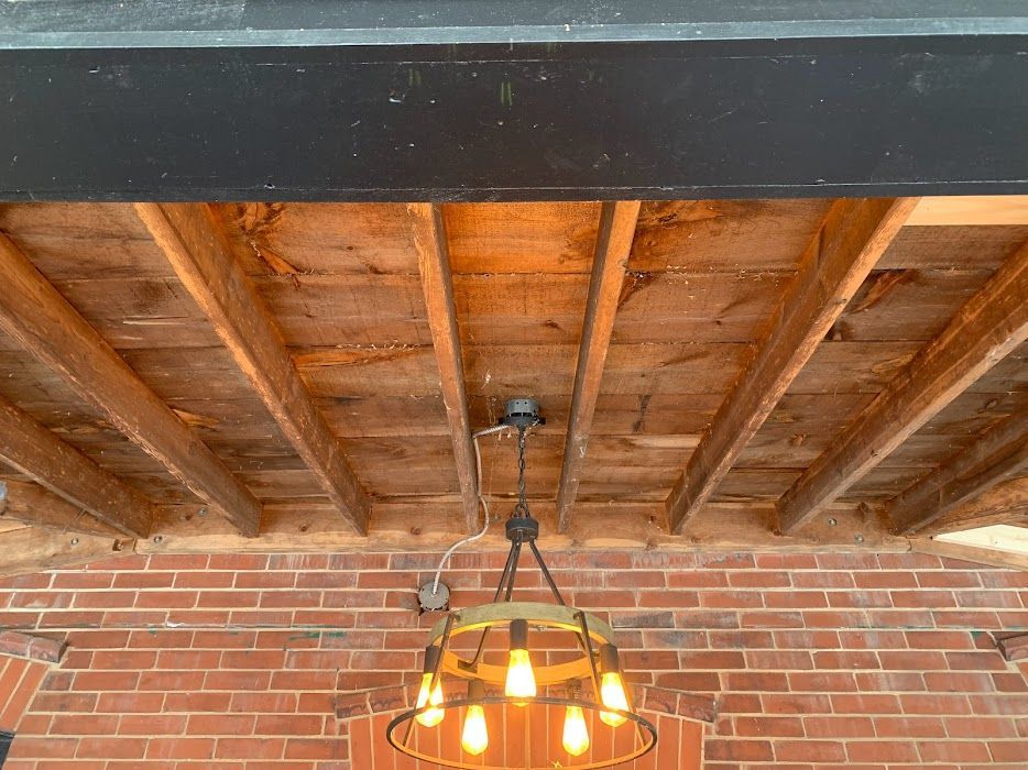 Exposed wood ceiling above a red brick wall with a hanging light fixture and black beam.