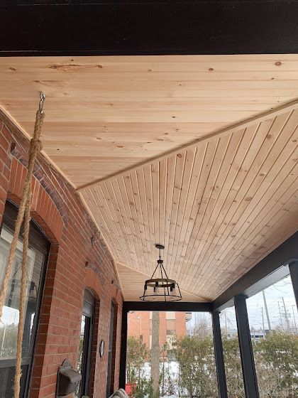 Wooden ceiling of a porch with a hanging light fixture, visible brick wall and black frame.