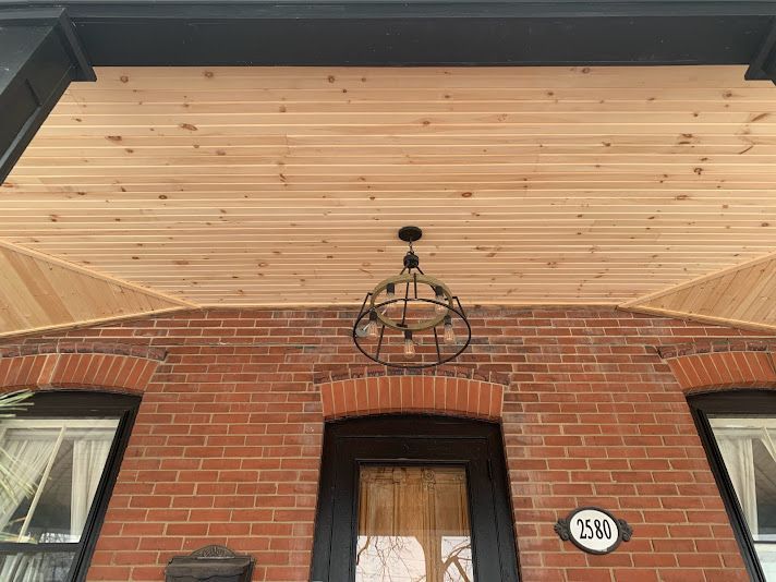 Brick facade with wooden porch ceiling, arched door, and decorative light fixture.