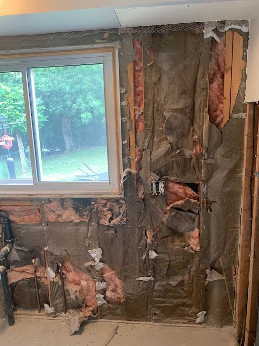 Wall with exposed insulation, electrical box, and window in a room undergoing renovation.
