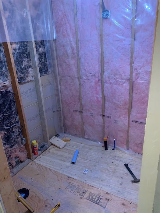 Construction of a shower stall with wood framing, insulation, and plumbing.