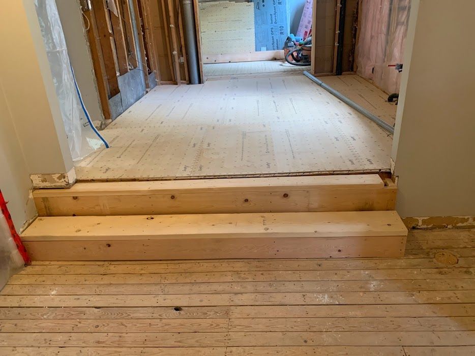 Wooden steps leading up to a room under renovation with exposed beams and unfinished flooring.