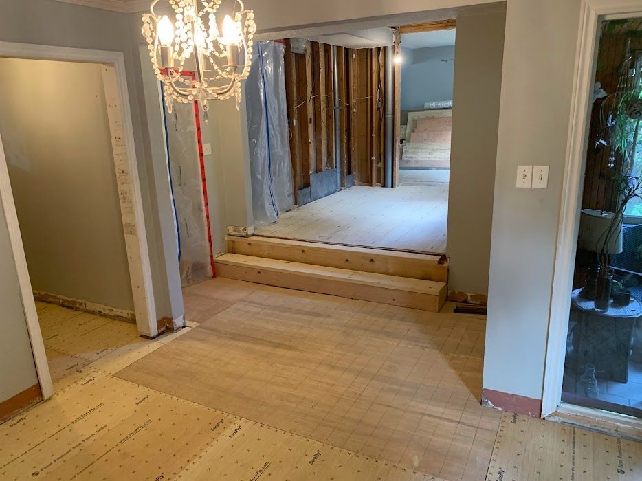 Renovation in progress: doorway with steps, exposed wall studs, and new wooden floors in a house.