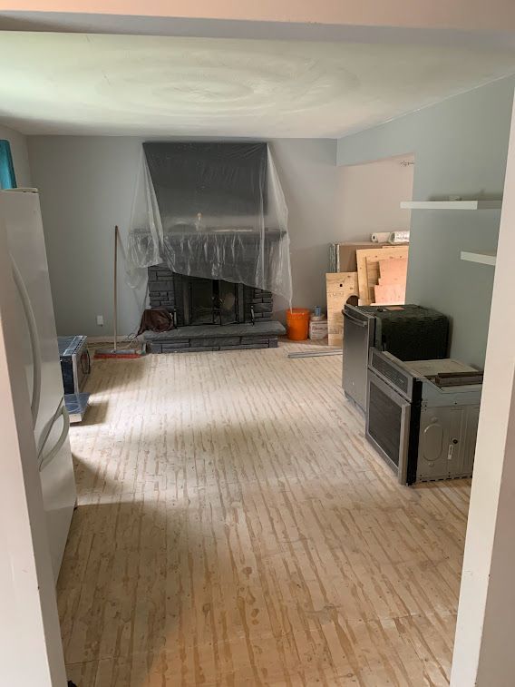 Room under renovation with gray walls, fireplace covered in plastic, and exposed wooden floors.