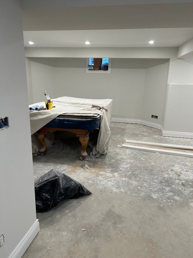 Basement room with a covered pool table, debris on the concrete floor, and unfinished walls.